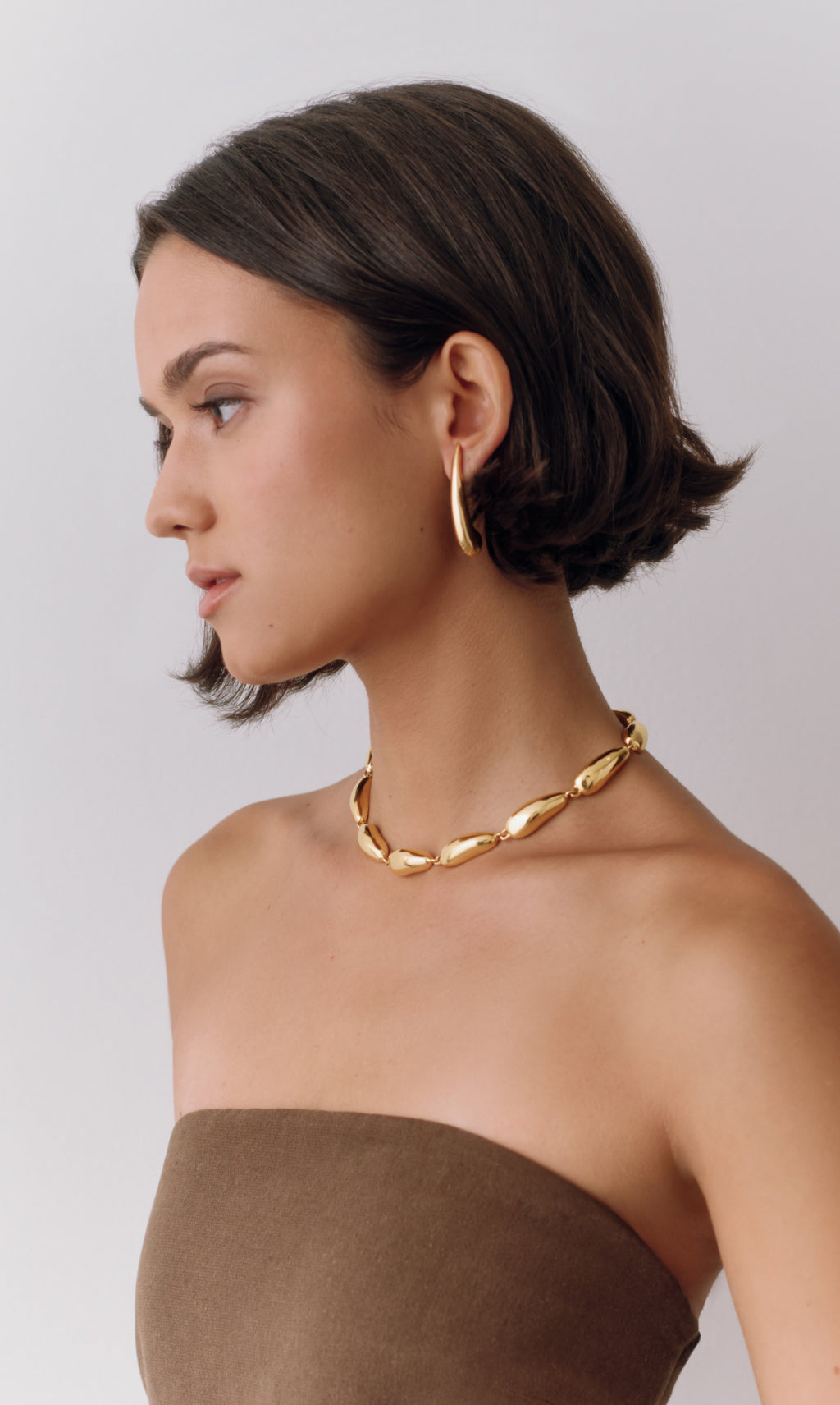 Person wearing a strapless top, large chain necklace, and hoop earrings.