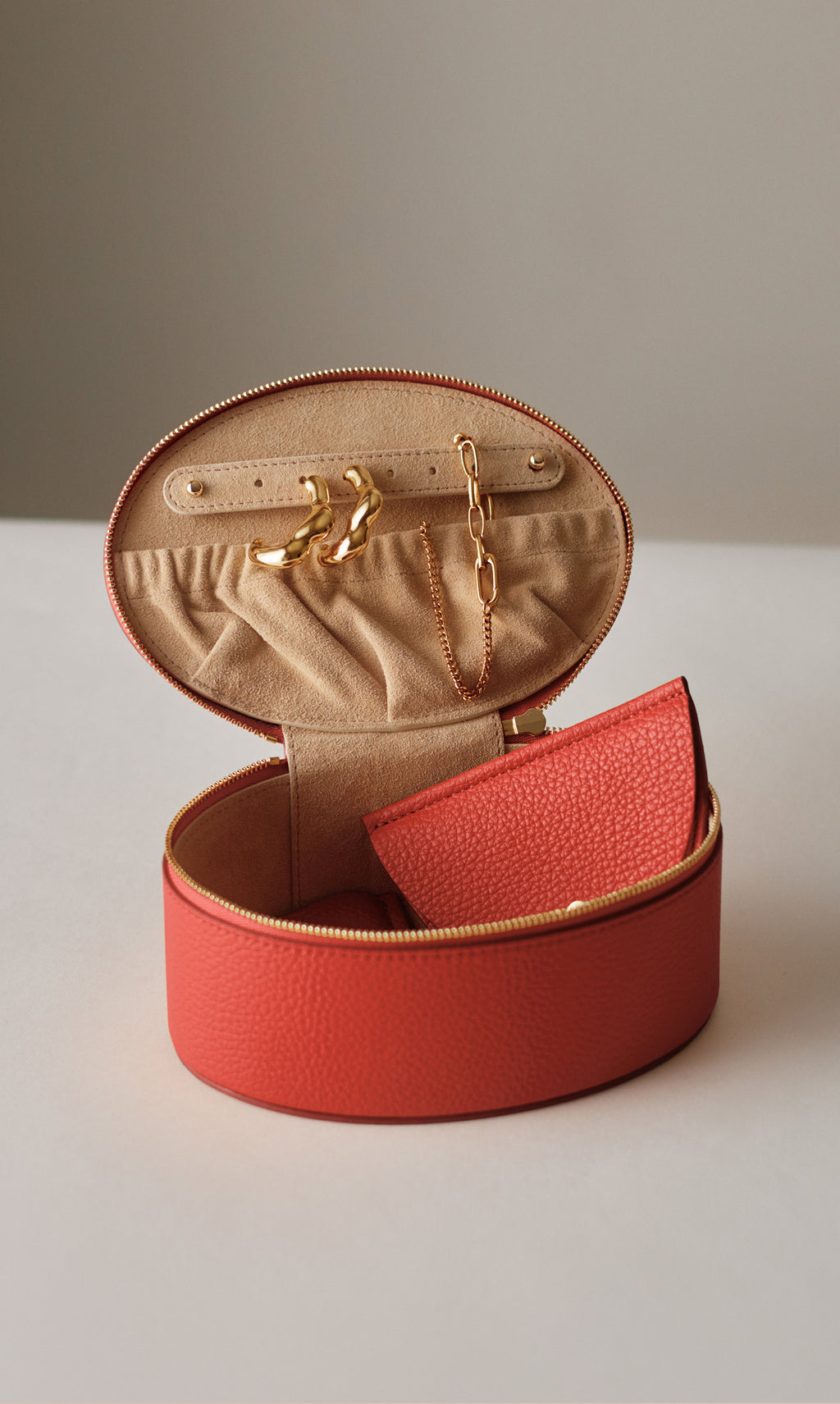 Oval jewelry case with open lid, holding earrings, chain, and a textured pouch.