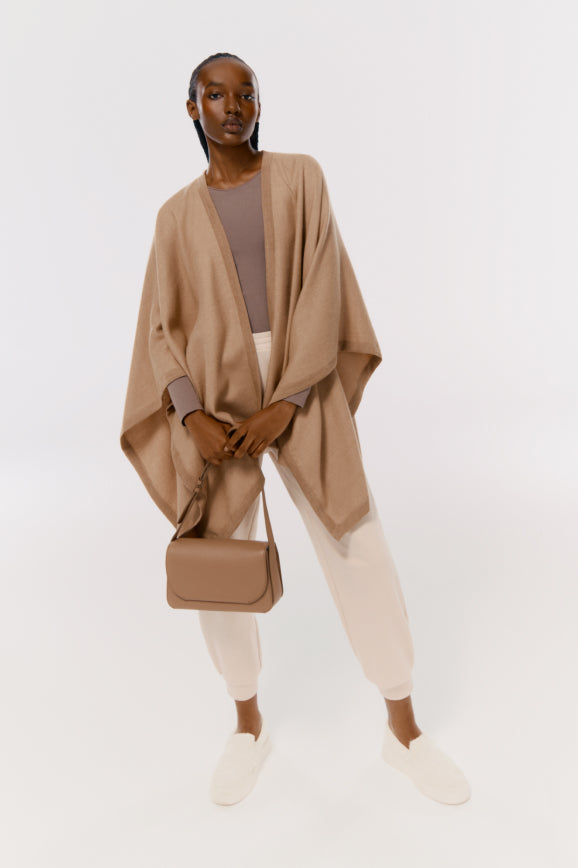 Woman standing in a studio wearing casual outfit and holding a handbag.