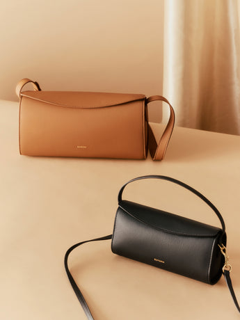 Two handbags with shoulder straps on a beige surface.