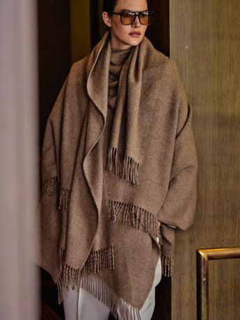 Person wearing a cape and glasses stands near a wall