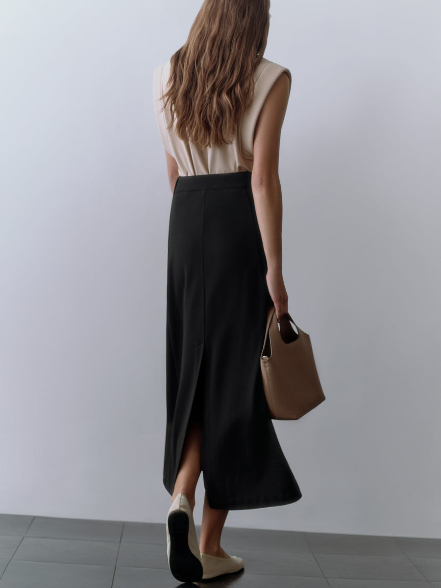 Person in long skirt holding a handbag, standing on tiled floor.