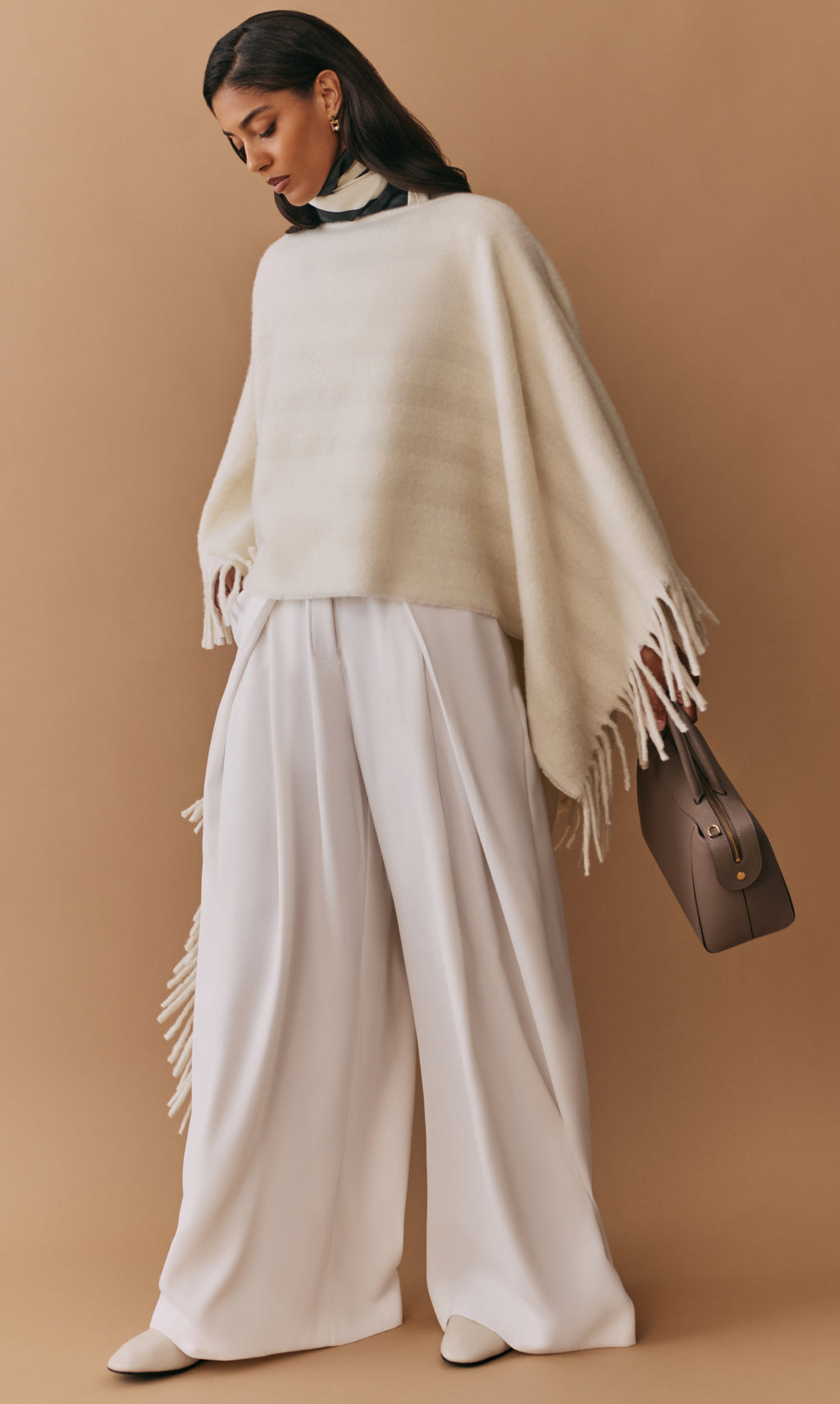 Woman in a cape and wide-leg pants holds a handbag