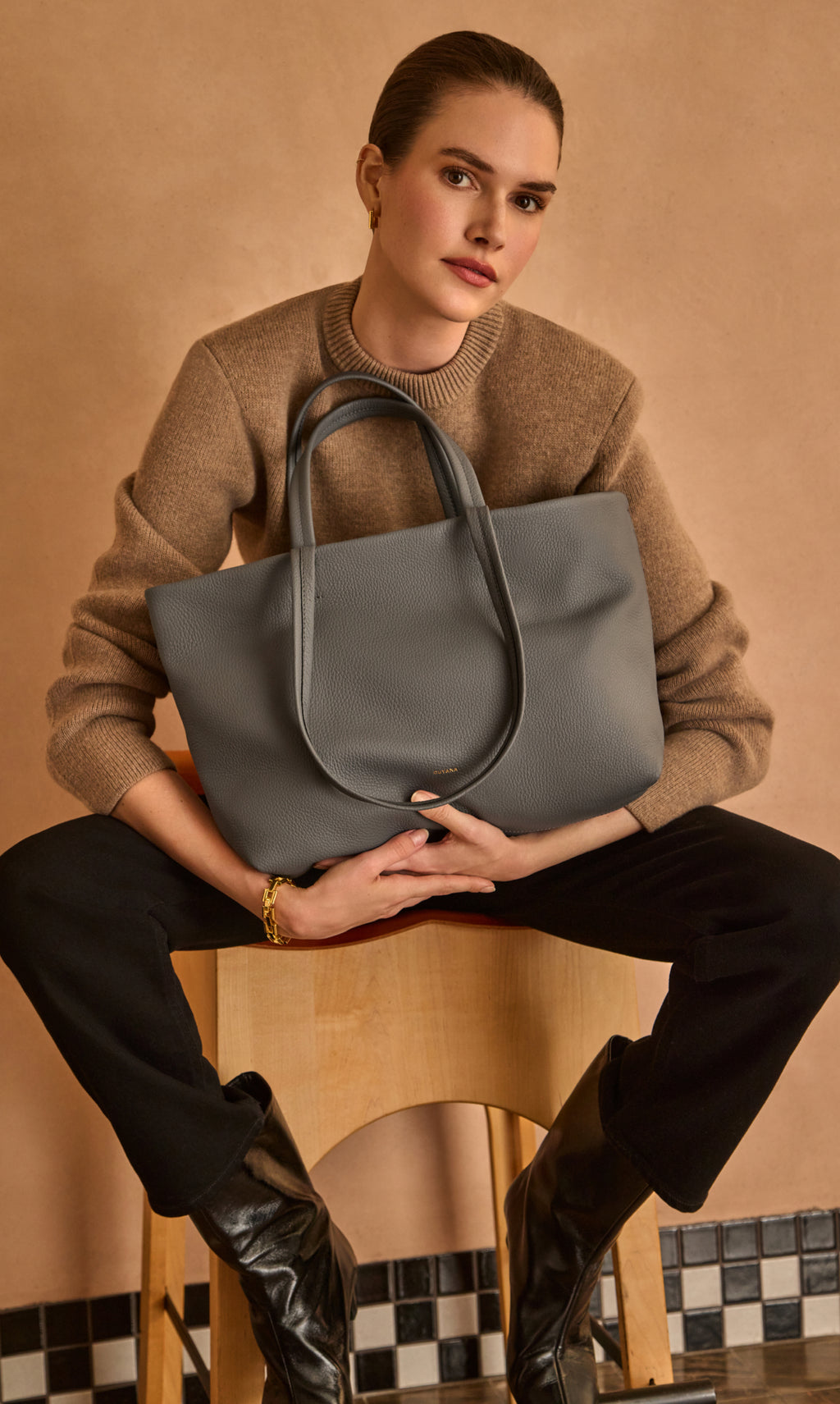 A person sitting on a stool holding a large tote bag.