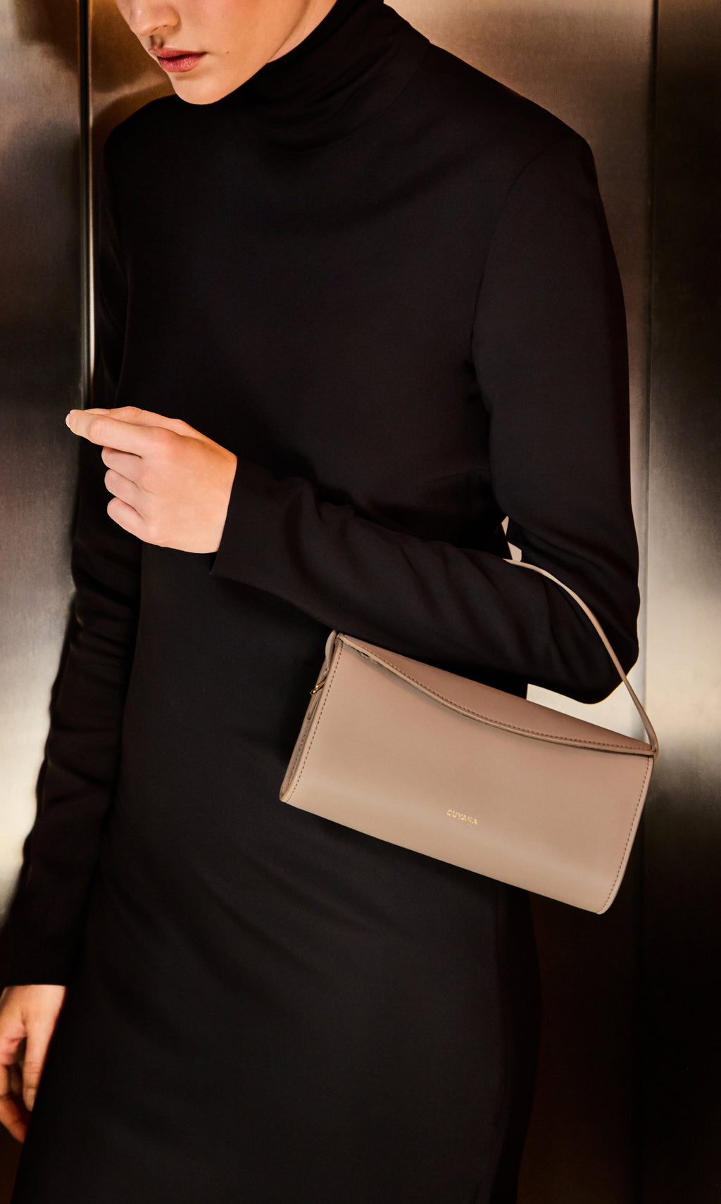 Person in long-sleeve outfit holding a small handbag in one hand.