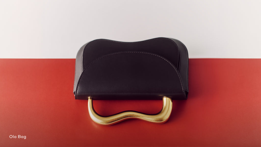 A handbag with a curved metal handle on a two-toned background.