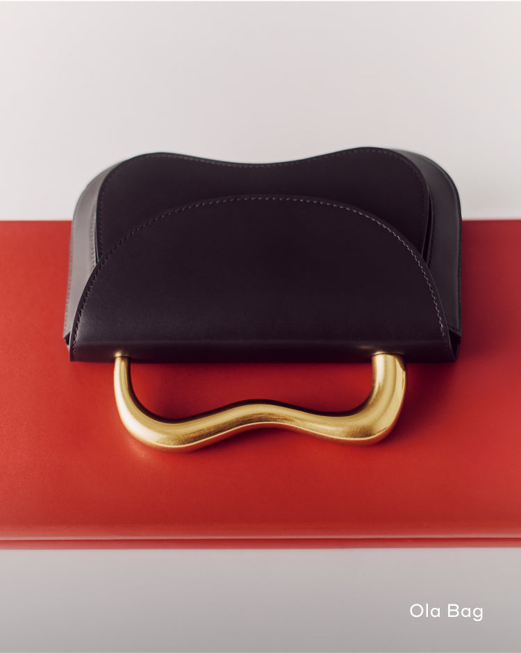 Handbag with curved gold handle on red surface