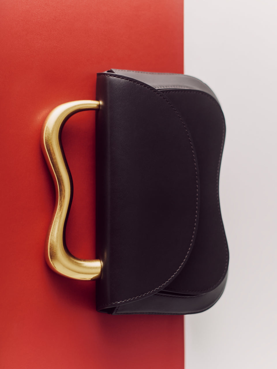 Purse with a curvy gold handle on a red and white background.