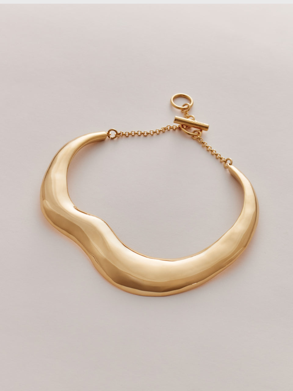 Wavy metal necklace with a hook clasp on a flat surface