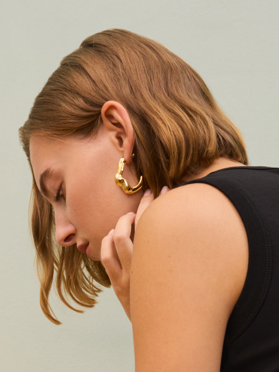 Person wearing a sleeveless top and large hoop earring, looking down.