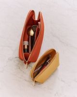 Two open zippered pouches with makeup brushes inside on a marble surface.