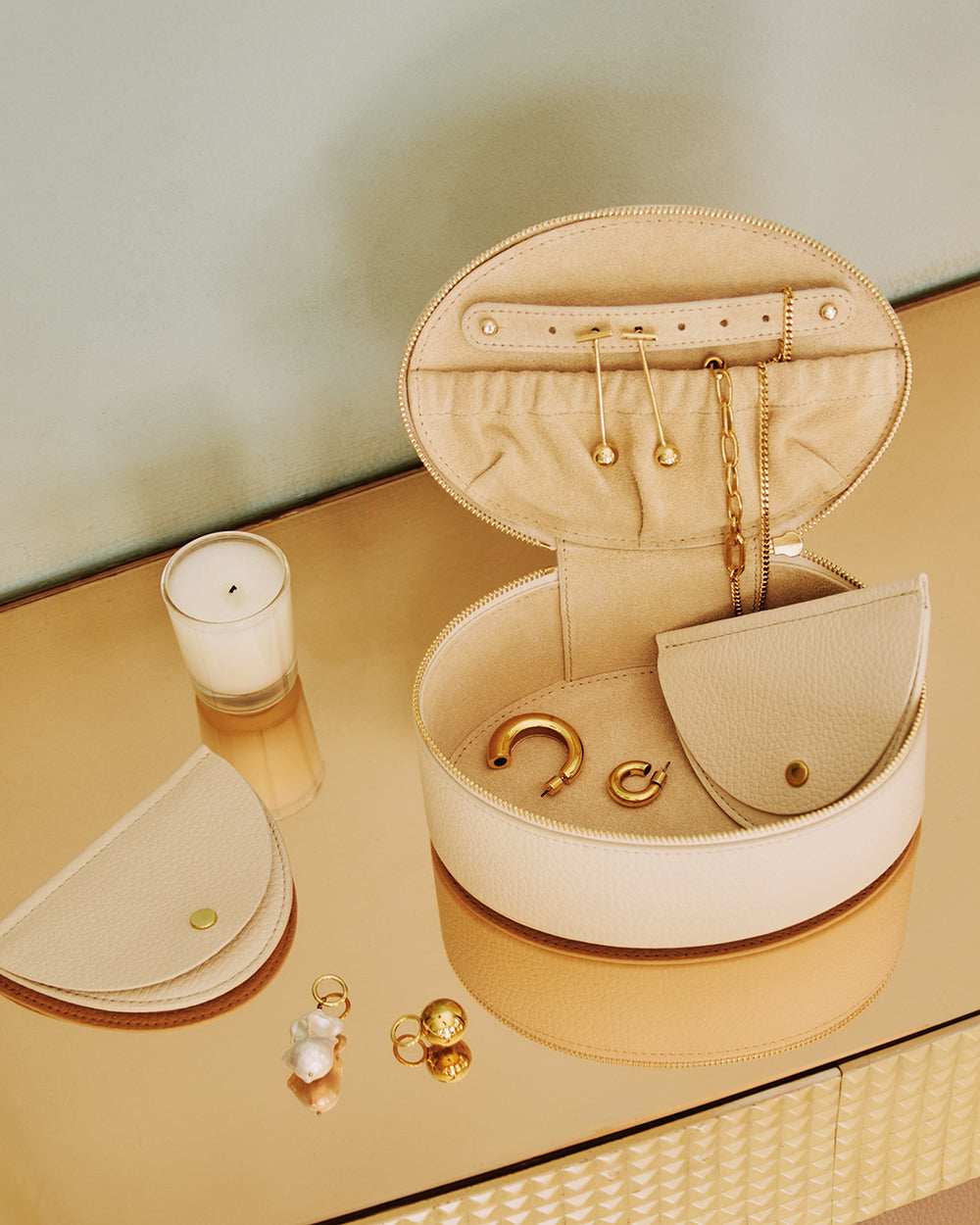 Jewelry box with earrings and necklaces beside a candle and small pouch on a table.