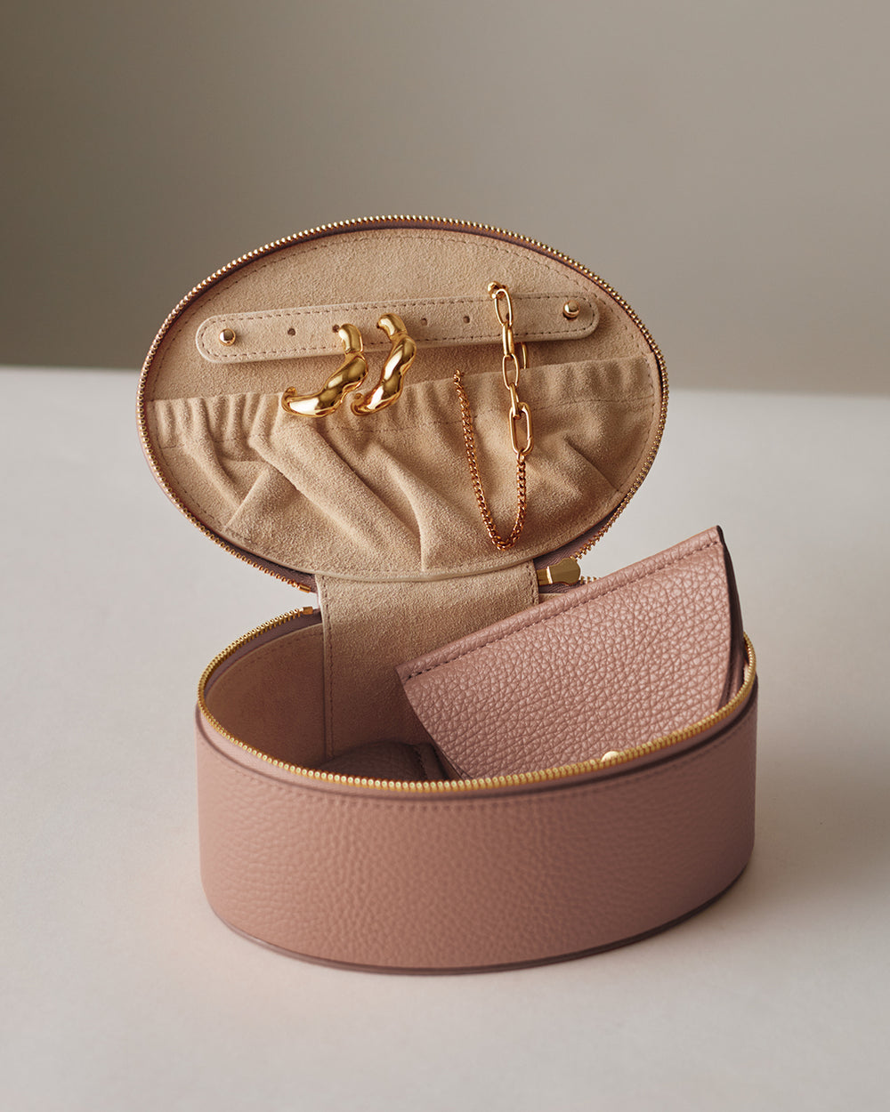 Small open travel jewelry case with earrings and a necklace, holding a textured wallet.