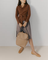 Person wearing a wrap top and skirt holds a large backpack