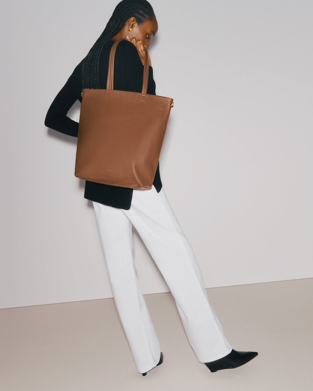 Person holding a large shoulder tote bag, wearing a long sleeve top and pants.