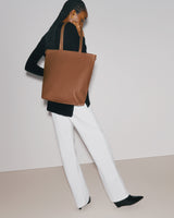 Person holding a large shoulder tote bag, wearing a long sleeve top and pants.