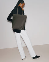 Person carrying a large tote bag, wearing a long-sleeve top and pants.