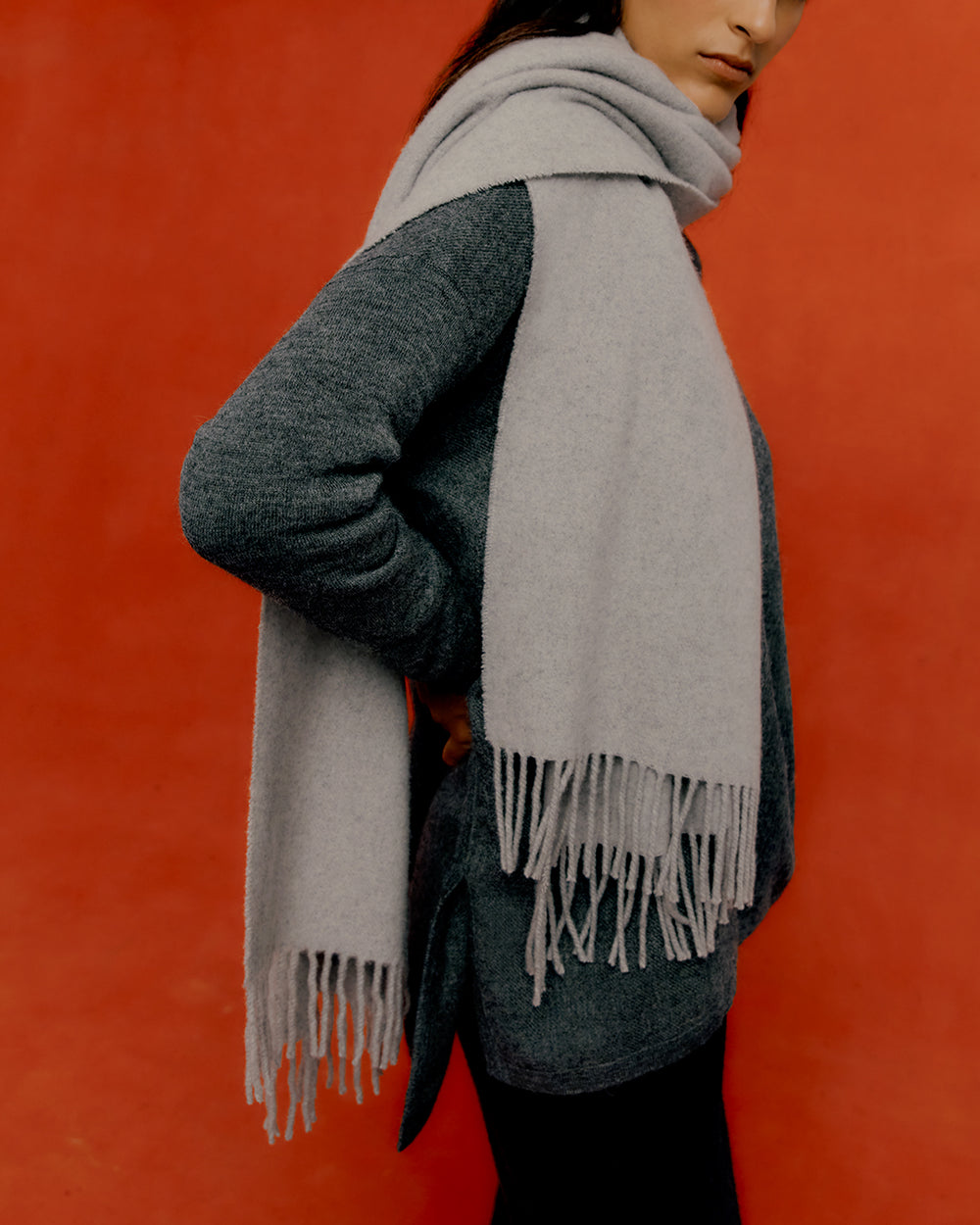 Person wearing a long scarf and sweater against a red background