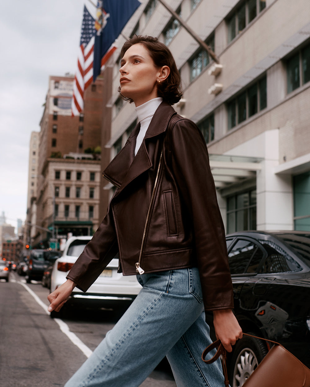 Person walking on a city street carrying a travel bag, wearing a jacket and jeans.