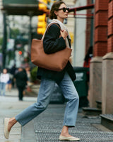 Person in a blazer and jeans carrying a large tote bag on a city street.