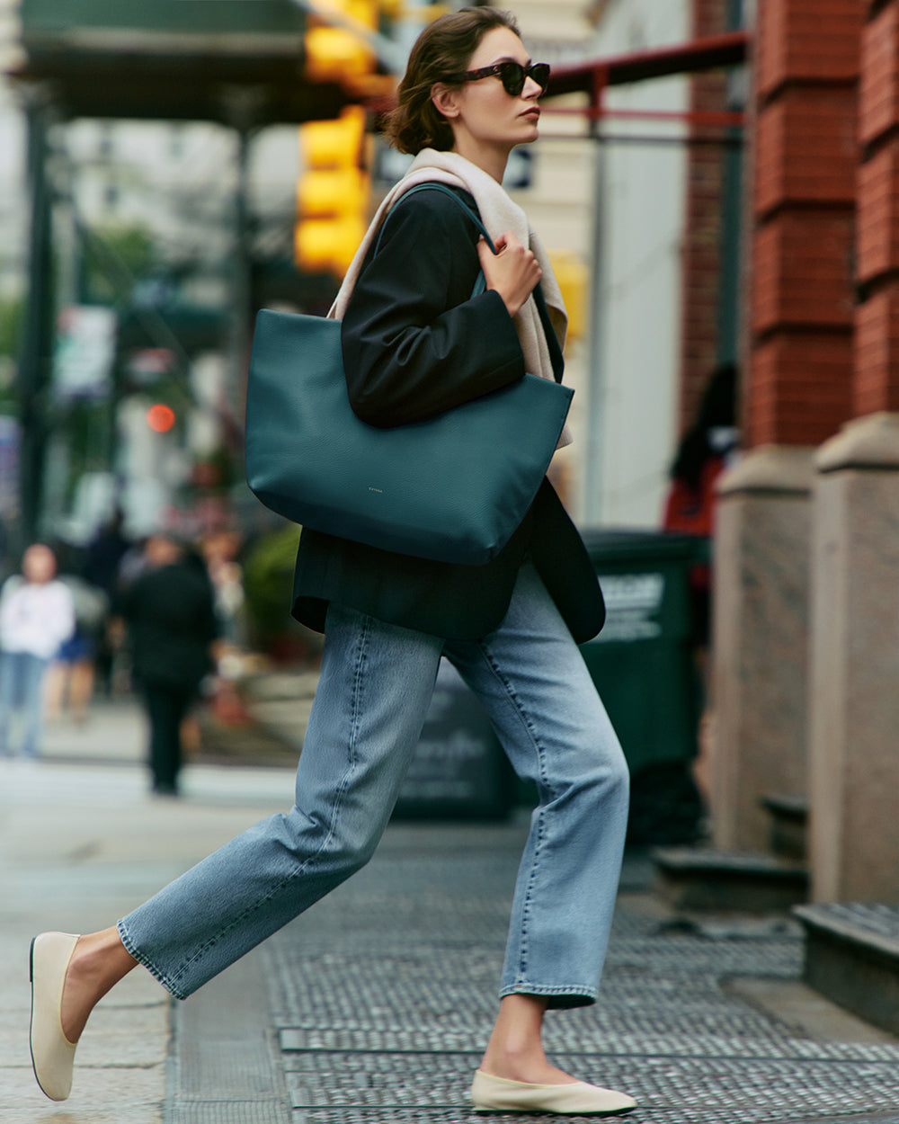 Person in a blazer and jeans carrying a large tote bag on a city street.