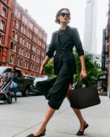 Woman in a city street carrying a large handbag and wearing sunglasses and a belt.