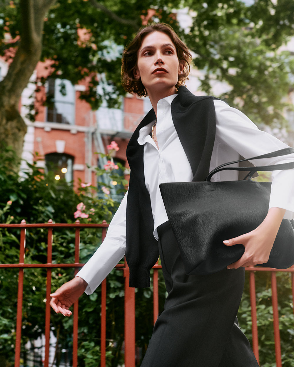 Person walking with a large handbag outdoors near a fence and trees.