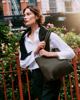 Person walking with a large handbag outdoors near a fence and trees.
