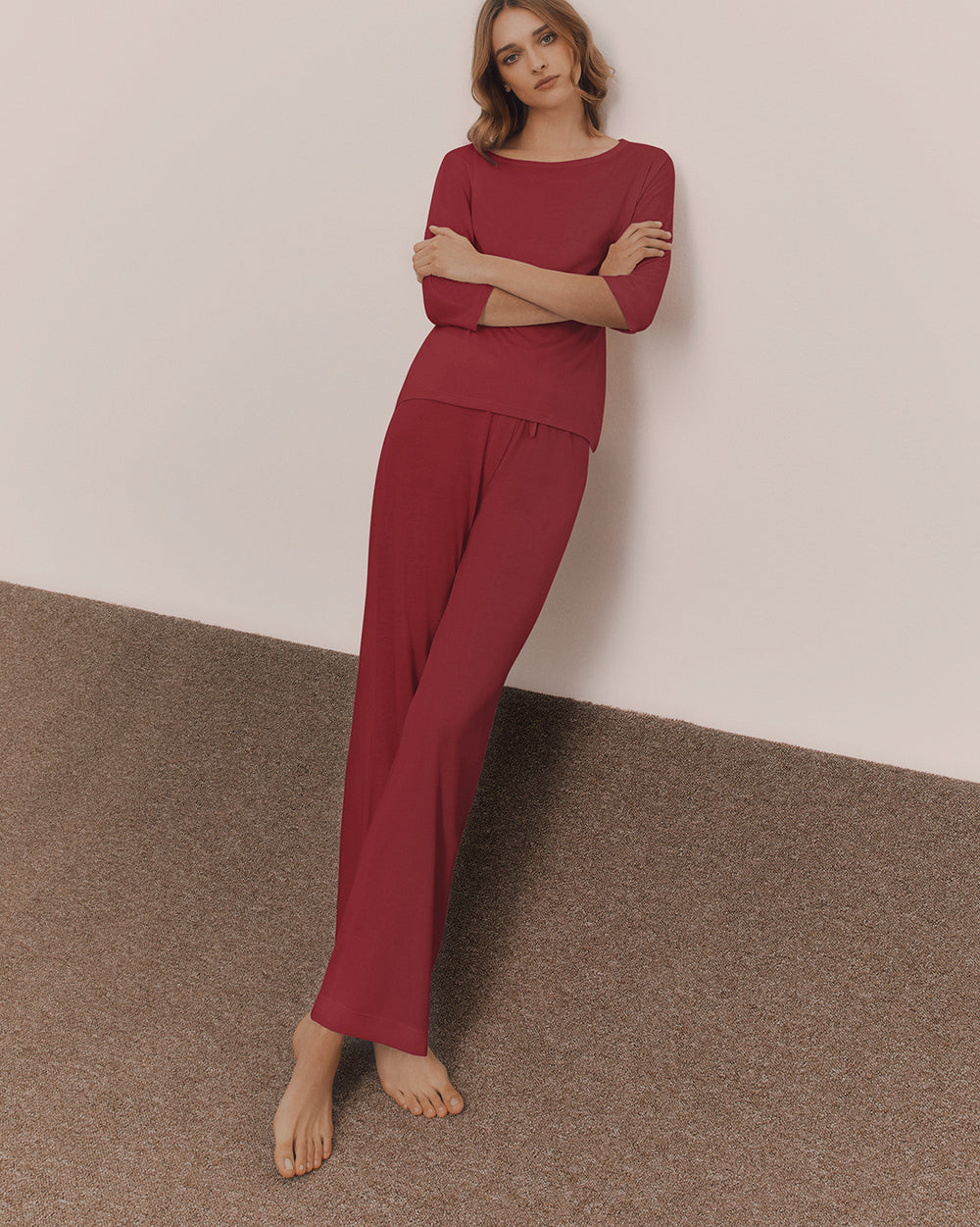 Person in relaxed clothing leaning against a wall with arms crossed.