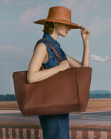 Person in denim dress holding large tote, with an airplane in the background.