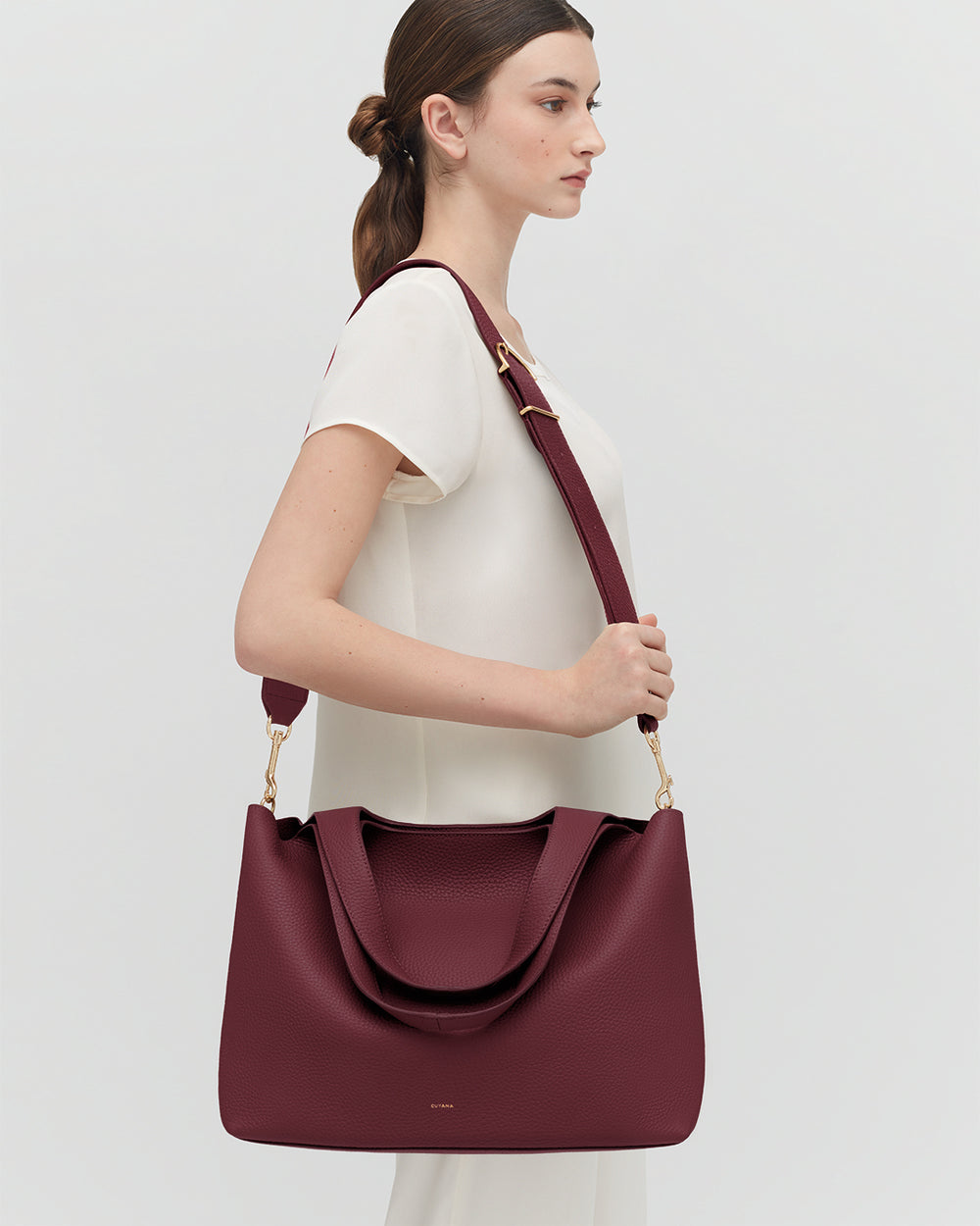 Woman holding a large handbag with a shoulder strap.