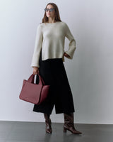 Person wearing sweater and wide-leg pants holding a large travel bag and wearing knee-high boots