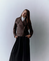 Person wearing a jacket and a long skirt, standing against a plain background.