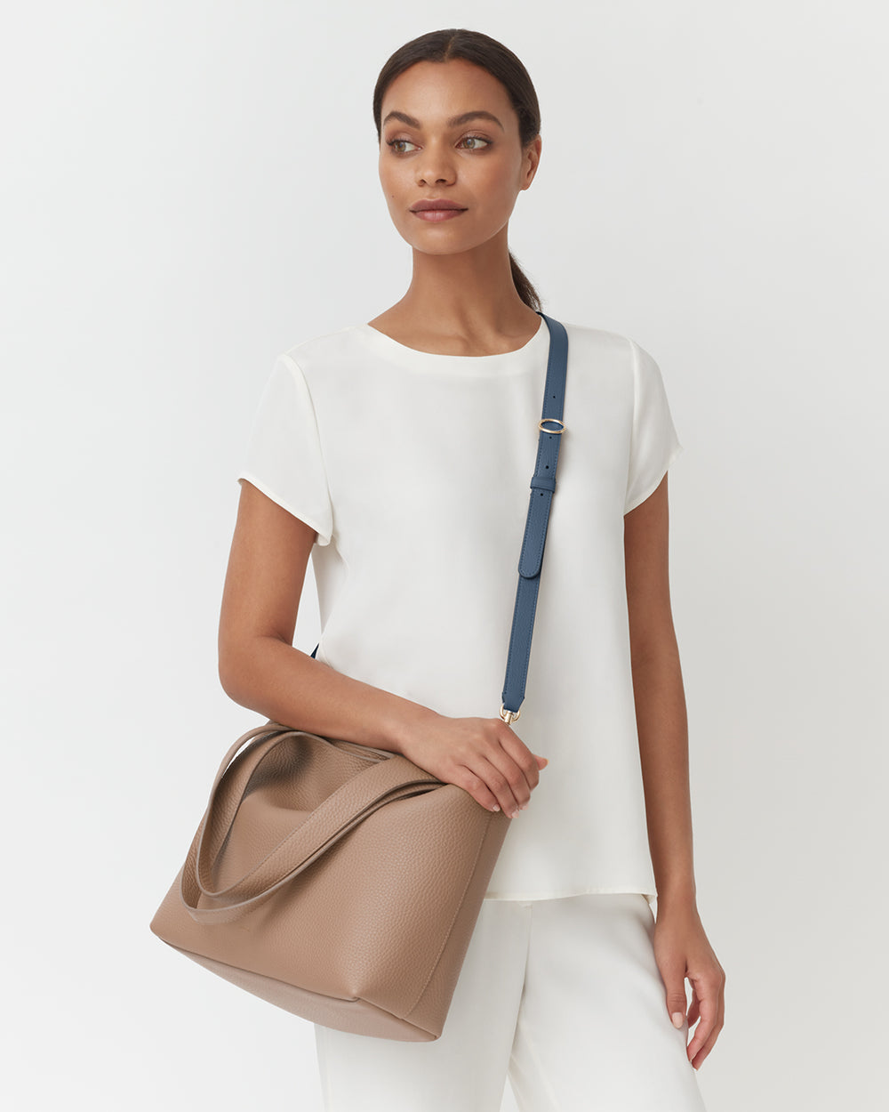 Person in a plain outfit holding a bag with a shoulder strap.