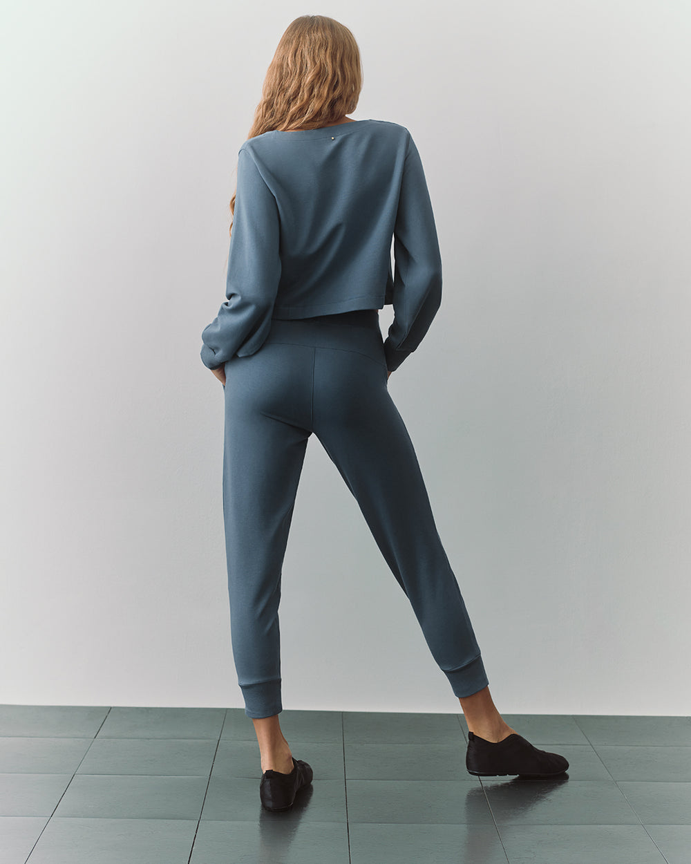 Person in matching long-sleeve top and jogger pants facing away on a tiled floor.