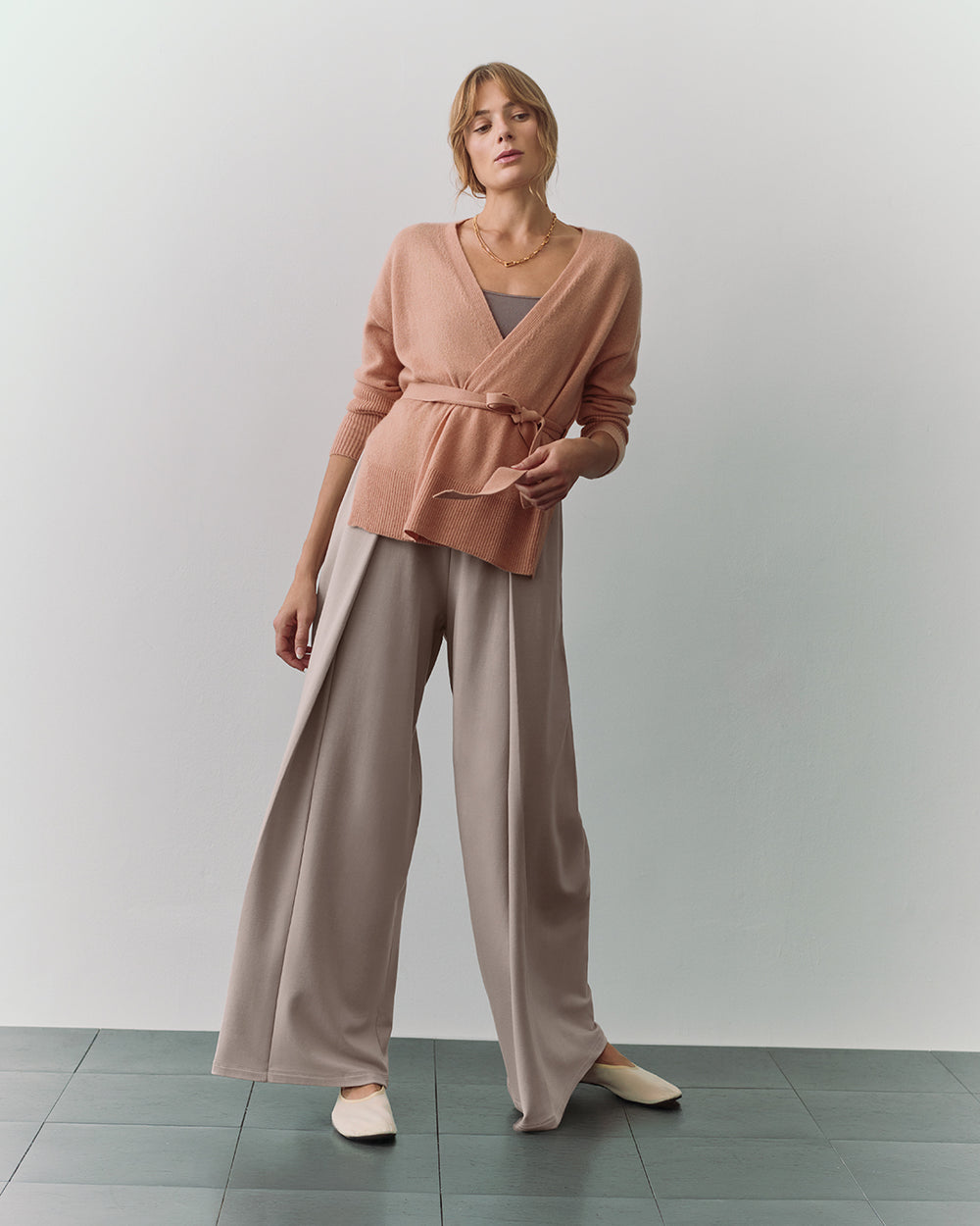 Person wearing wrap sweater and wide-leg pants standing on a tiled floor.