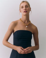 Person wearing a strapless top and gold necklace with a pearl charm.