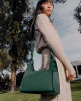 Person standing outdoors with a handbag over their shoulder.