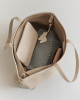 Open tote bag with a folded sweater, pouch, and a small keychain inside.