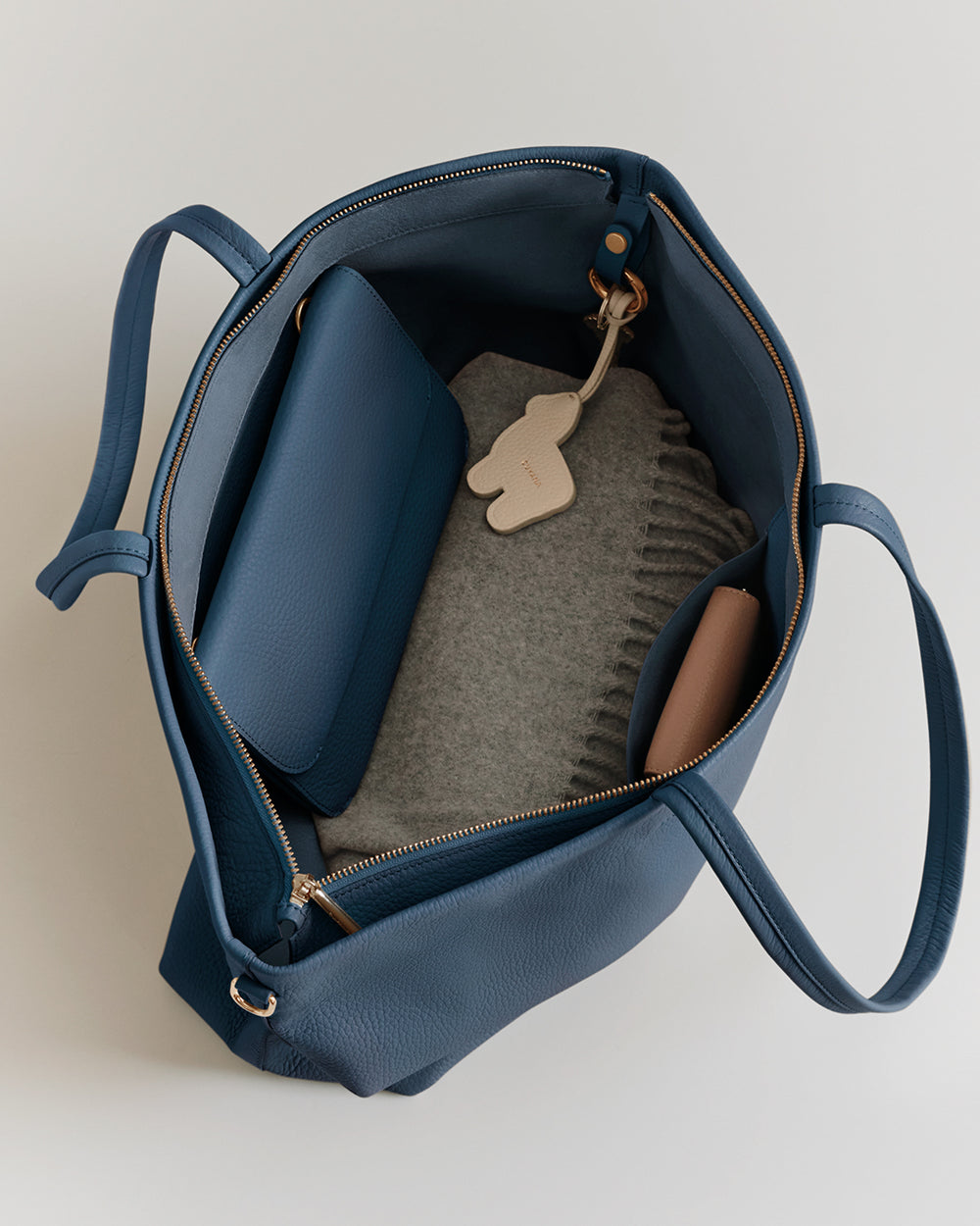 Open tote bag with a folded sweater, pouch, and a small keychain inside.