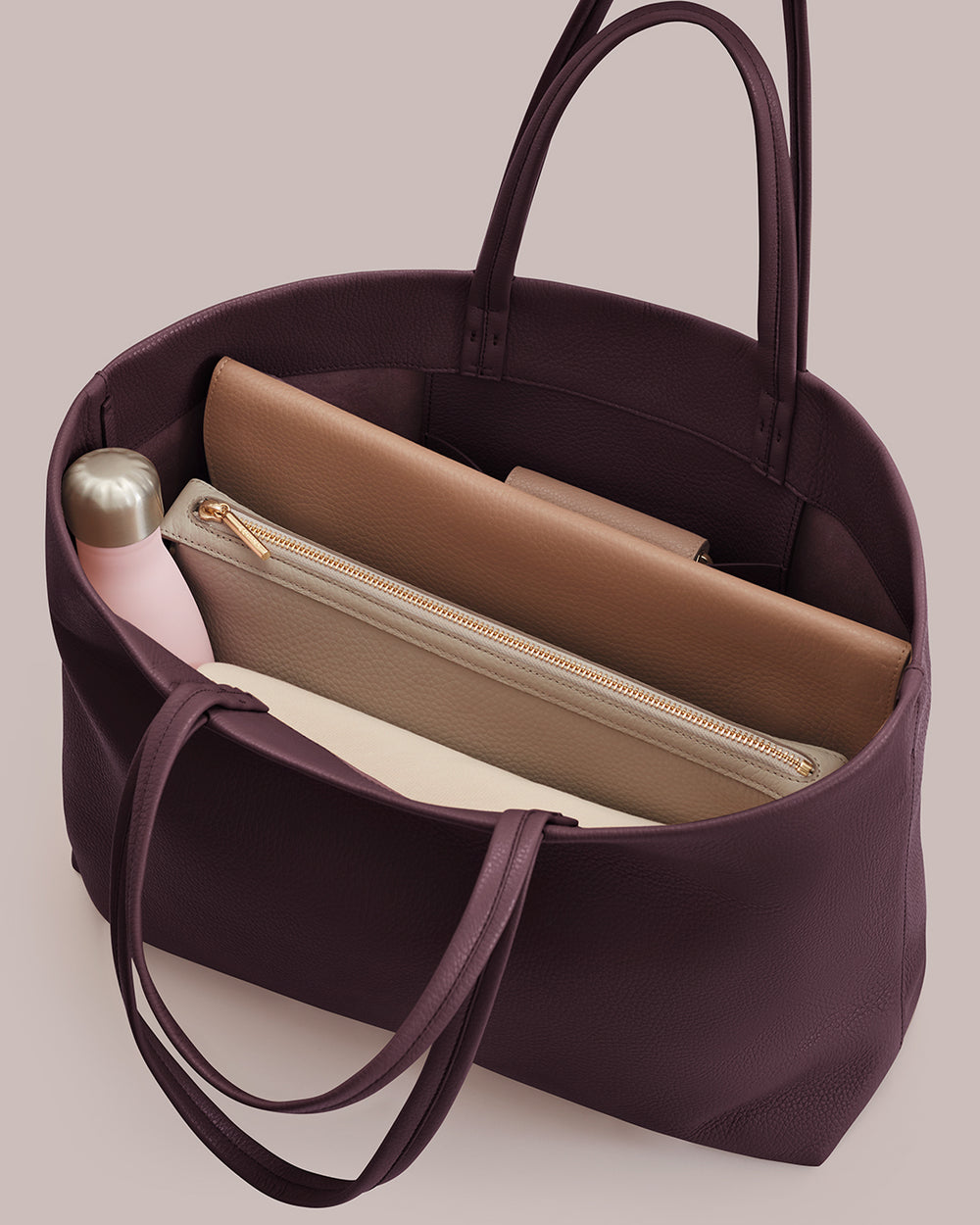 Open tote bag with a pink bottle and two zippered pouches inside.