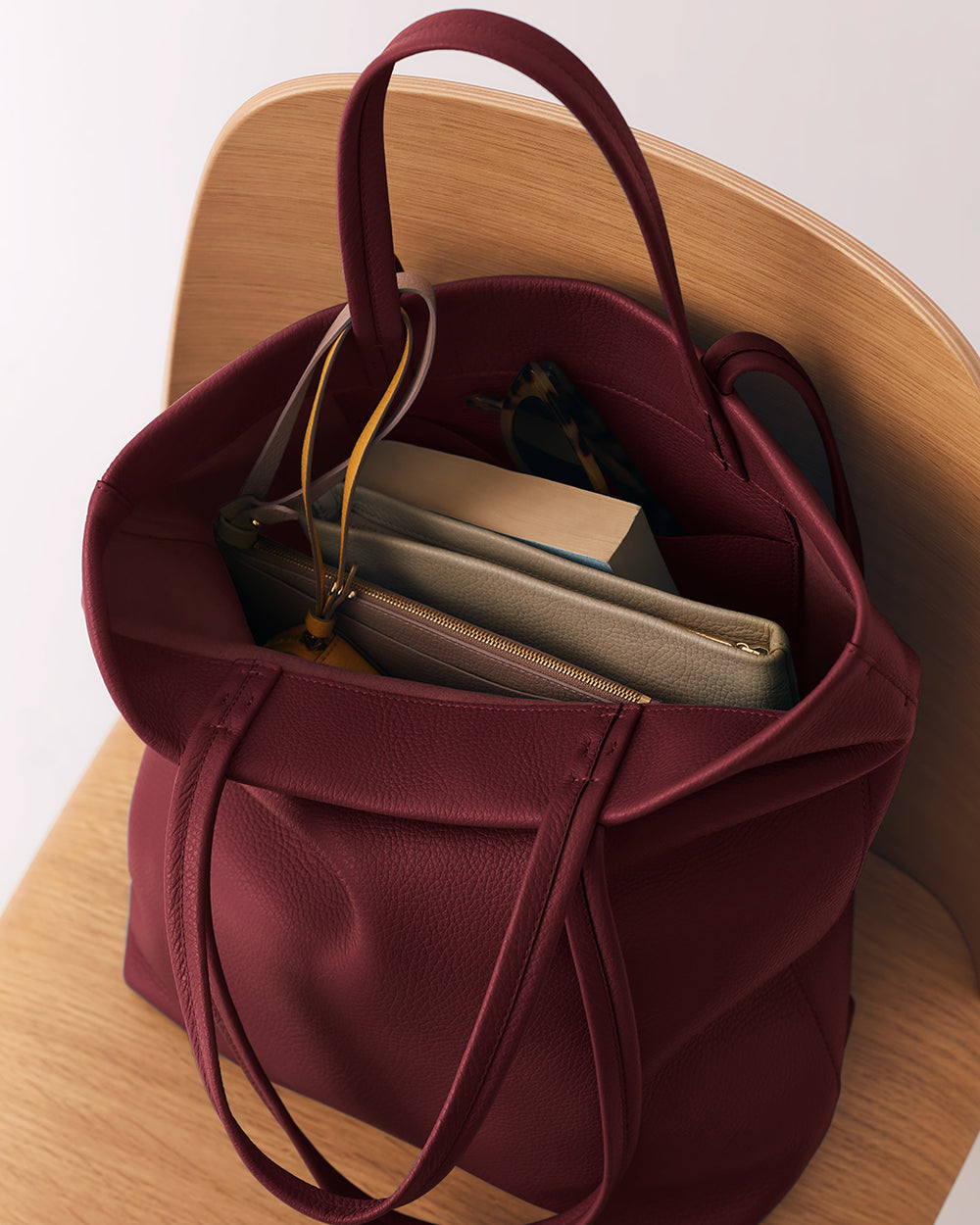 Open tote bag on a chair containing books and a pair of sunglasses