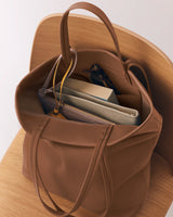 Open tote bag holding books and folders on a wooden chair