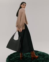 Person standing on green rug holding a large shoulder bag, wearing a long skirt and heeled boots