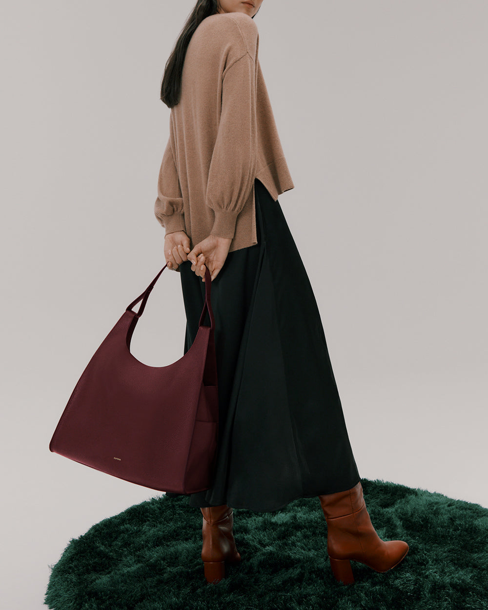 Person holding a large handbag wearing a sweater, long skirt, and high boots.