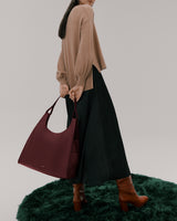 Person holding a large handbag wearing a sweater, long skirt, and high boots.