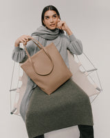 Woman in a sweater and skirt holding a handbag, sitting on a chair.