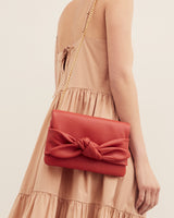 A person holding a purse with a chain strap and bow detail.
