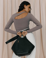 Woman standing with her back to the camera holding a bag.