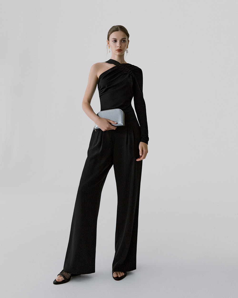 Woman in elegant one-shoulder top and trousers holding a clutch.